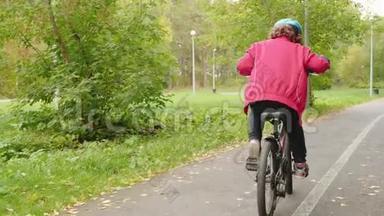 骑自行车的男孩骑自行车在秋季公园后景的道路上。 少年男孩骑在滑板上。 后视图二
